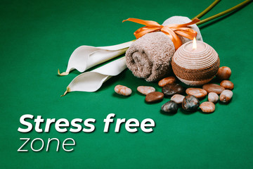 Spa essentials, candle, stones, towel and flowers on a dark green background