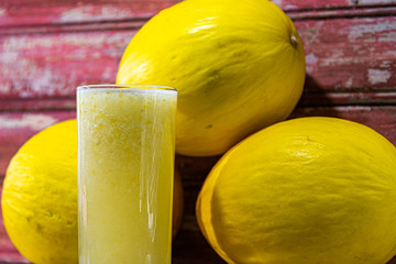 Spanish melon juice (Cucumis mello) and fruits on aged red wooden background