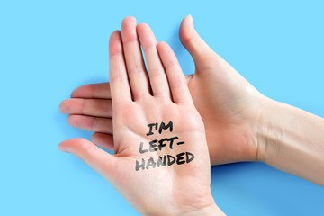 Female left hand with the words I am left-handed isolated on a blue background, celebration of left-handed day
