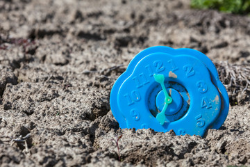 Broken toy clock at the bottom of a dried lake. Time concept. Selective focus, place for text.