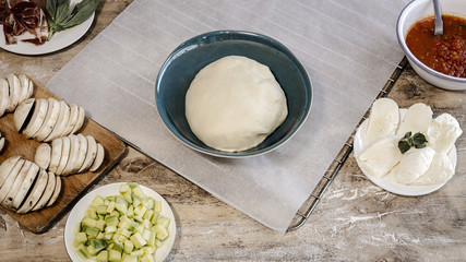 Cook hands making pizza dough and preparing with tomato, mushrooms, ham, mozzarella and parmesan cheese.