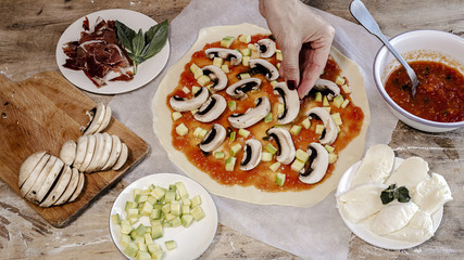 Cook hands making pizza dough and preparing with tomato, mushrooms, ham, mozzarella and parmesan cheese.