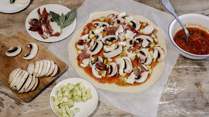 Cook hands making pizza dough and preparing with tomato, mushrooms, ham, mozzarella and parmesan cheese.