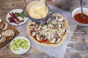Cook hands making pizza dough and preparing with tomato, mushrooms, ham, mozzarella and parmesan cheese.