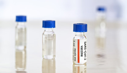 Coronavirus Covid 19 vaccine concept - small glass vials with blue caps on white table, closeup detail (own sticker design with dummy data - not real product)