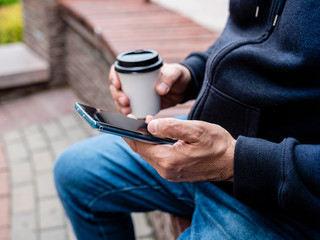 Fototapeta premium Close-up of hands of a man with coffee in a paper Cup and a smartphone.