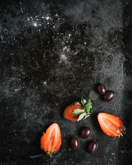 Truskawki i winogrona na czarnym stole, widok z góry. 