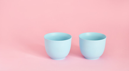 minimalism concept with light pastel colored blue cups on pink background.