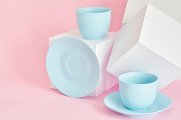 minimalism concept with light pastel colored blue cups and plate with white paper cubs on pink background.