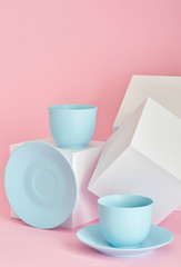 minimalism concept with light pastel colored blue cups and plate with white paper cubs on pink background.