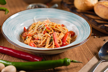 Pasta with tomatoes and peppers, and parmesan cheese in a blue plate on a wooden table