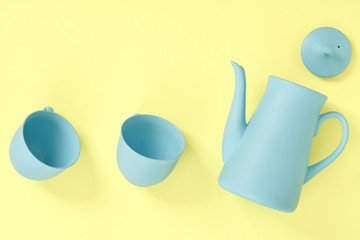 minimalism concept with light pastel colored blue teapot and cups on yellow background.  Flat lay. Tea time concept. Empty space