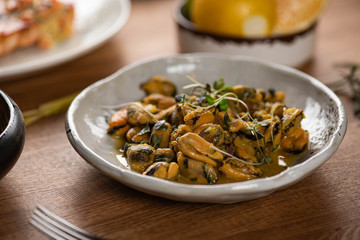 stewed mussels in souse with microgreens and lemon in a white deep plate on a wooden table