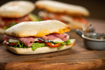 panini or hot sandwiches with beef, ham, herbs and cheese, tomatoes and red pepper on a wooden cutting board