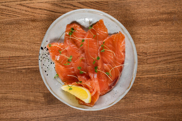 pickled salmon with microgreens and lemon on a wooden table. top view