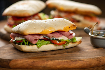 panini or hot sandwiches with beef, ham, herbs and cheese, tomatoes and red pepper on a wooden cutting board