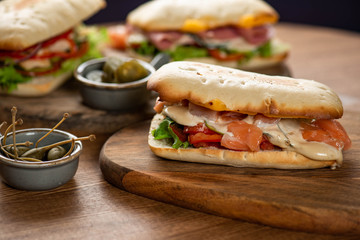 panini or hot sandwiches with beef, ham, herbs and cheese, tomatoes and red pepper on a wooden cutting board