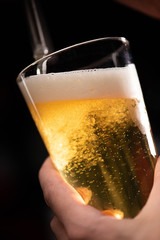 light beer on tap beer is poured into a glass that holds man's hand on a black background, close-up