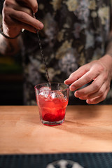 bartender stirs the cocktail Campari tonic with a spoon in glasses on a black bar counter