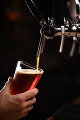 dark beer on tap beer is poured into a glass that holds man's hand on a black background, copy space