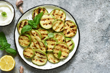 Grilled zucchini with sauce on concrete background. View from above.