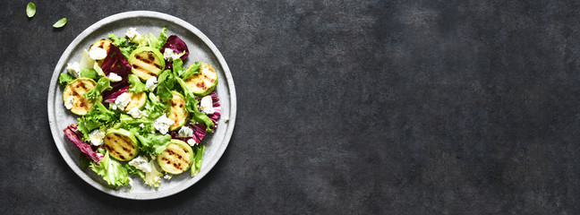 Mix salad with grilled zucchini and sauce on a black background.Top view with copy space.