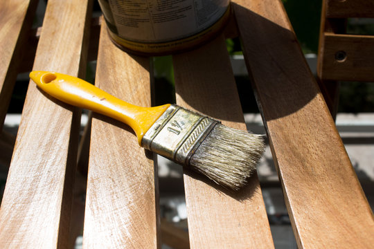 Applying varnish on wood table chair finish painting with tin and yellow paint brush in open air do it yourself diy make at home take a hobby keep busy with brush detail tin in background balcony