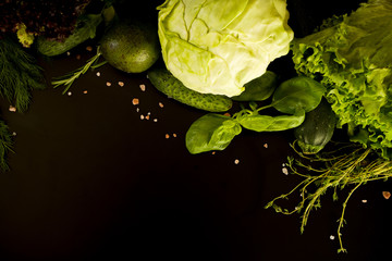 Frame of assorted fresh vegetables on a dark background with a place for text. Top view on the basil, thyme, rosemary, cabbage, cucumber, avocado, zucchini.