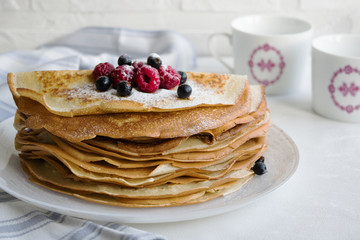 A stack of pancakes with fresh berries and icing sugar. The background is light, side view, horizontal orientation.