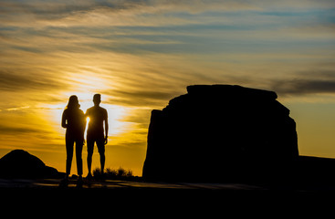 Silhouette of people in Monument Valley at sunrise with butte and clouds in background.