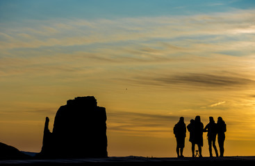 Fototapeta na wymiar Silhouette of people in Monument Valley at sunrise with butte and clouds in background.