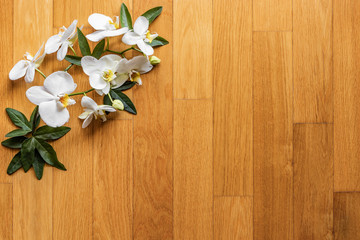Texture, background with white orchid flowers and green leaves on a wooden surface (parquet, wooden strips). Rustic, vintage, natural, traditional, grunge, summer, spring concept.