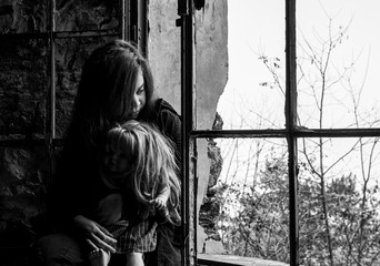 young woman alone holding favourite doll looking through window. Teen in depression