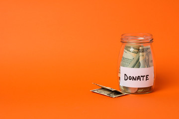 Glass jar with money and text Donate on orange background
