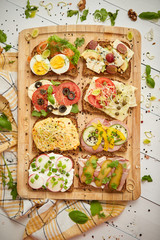 Colorful, different kinds sandwiches served on wooden chopping board. Vegetable toppings