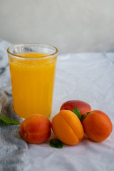 Ripe whole apricots and a glass of apricot juice on textile surface