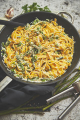 Tagliatelle pasta with ricotta cheese sauce and asparagus served on a black iron pan