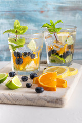 Summer healthy cocktails of citrus infused waters, lemonades or mojitos, with lime lemon orange blueberries and mint, diet detox beverages, in glasses on light background