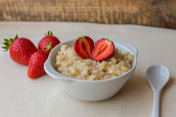 Oatmeal with strawberries in a white bowl. Healthy breakfast, vegetarian lifestyle concept