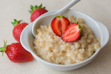 Homemade oatmeal with strawberries in a white plate. Healthy breakfast. Oatmeal with sliced ​​strawberries.