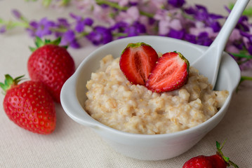 Oatmeal with strawberries in a white bowl. Healthy breakfast with oatmeal and fresh organic berries. Hot and healthy breakfast. Dietary nutrition. Top view, close up