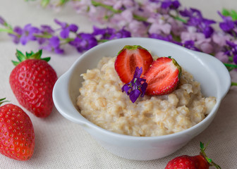 Oatmeal with strawberries in a white bowl. Healthy breakfast with oatmeal and fresh organic berries. Hot and healthy breakfast. Dietary nutrition. Top view, close up
