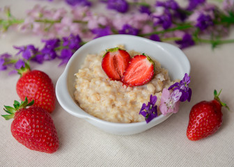 Oatmeal with strawberries in a white bowl. Healthy breakfast with oatmeal and fresh organic berries. Hot and healthy breakfast. Dietary nutrition. Top view, close up
