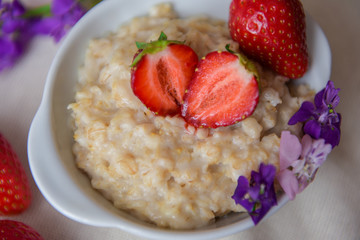Homemade oatmeal with strawberries in a white plate. Healthy breakfast. Oatmeal with sliced ​​strawberries.