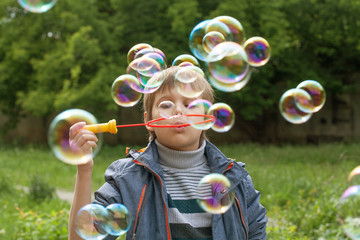 Little cute boy inflates soap bubbles in the park in nature, joyful emotions in a child, bright big...