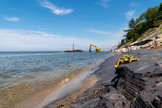 Child's construction toy on the beach with real construction equipment in the background