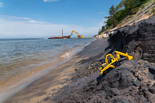 Child's construction toy on the beach with real construction equipment in the background
