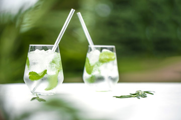 Beautiful glass of water or mojito with lime and mint cocktail on the gree background and white table summer vibe and atmosphere