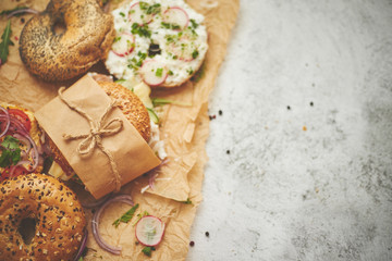 Bagels with ham, cream cheese, hummus, radish wrapped in brown baking paper ready for take away