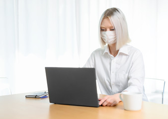 
A young girl works with a laptop at home or in the office. antiviral mask.